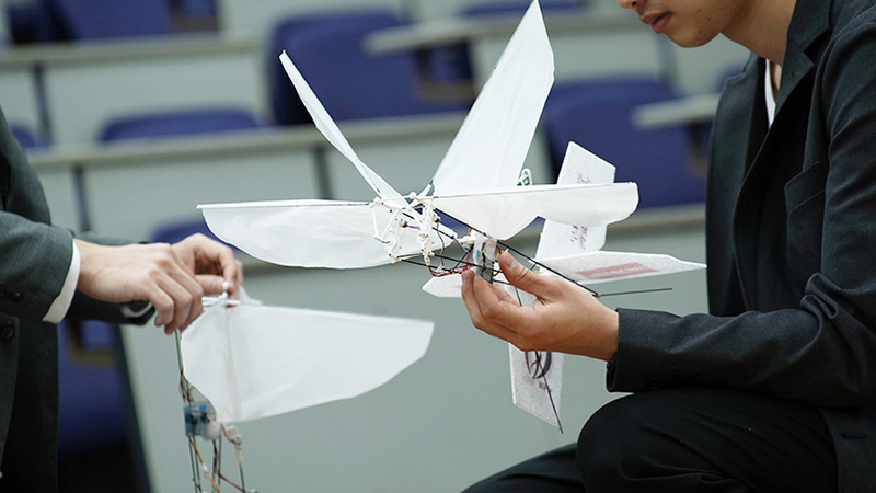 A man holds a white lightweight robot that has the shape of a dragonfly