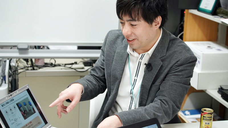 Yoshihiro Sejima sits at a desk and points to a laptop screen.