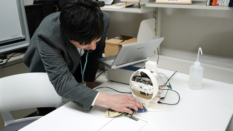 Yoshihiro Sejima uses a cloth to clean the base of the robot with eyes