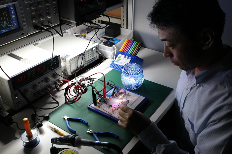 Taniguchi is sat in front of the desk working on his prototype device earable
